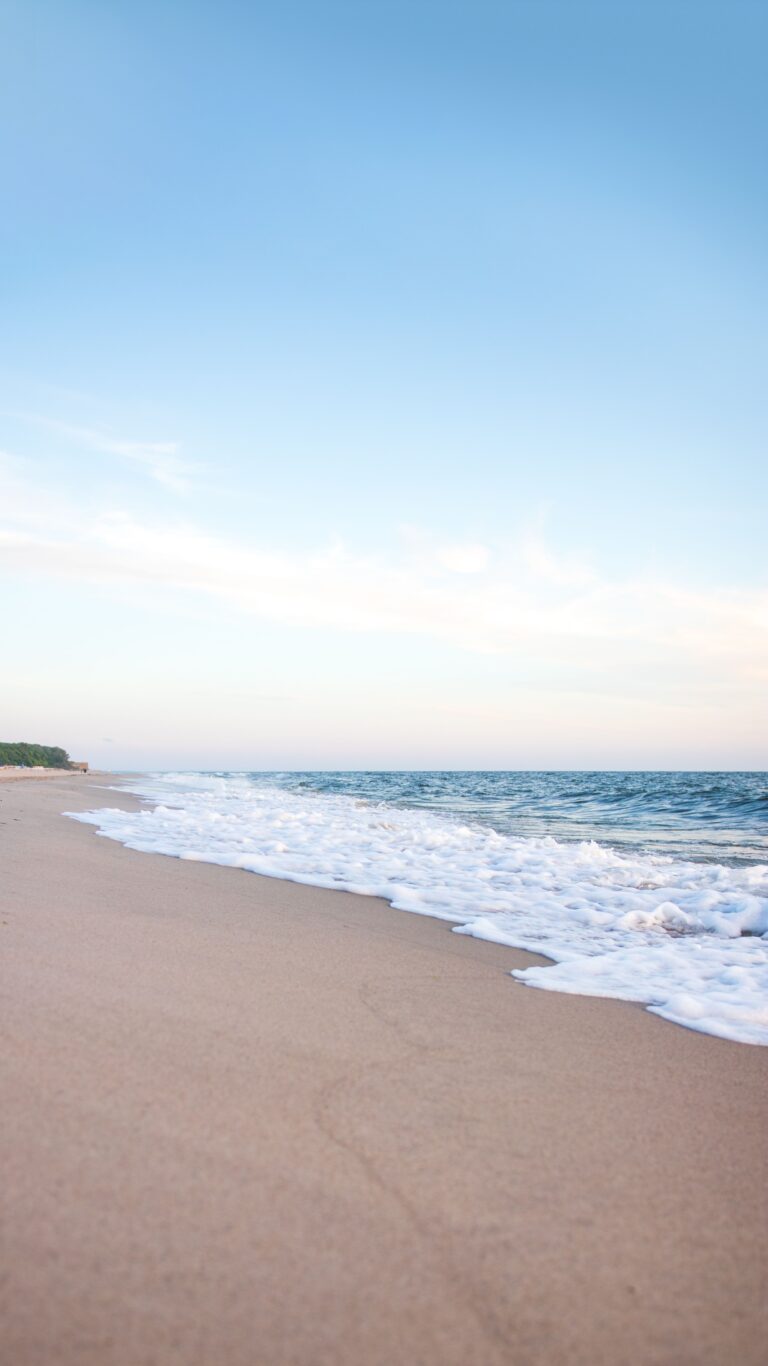 Gentle waves rolling onto a quiet sandy beach beneath a clear blue sky.